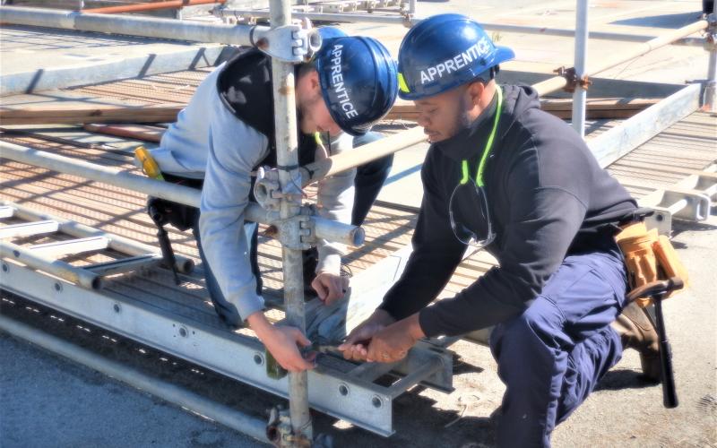 Two Kings Bay Trident Refit Facility apprentices work to set up scaffolding to support repair work on submarines.