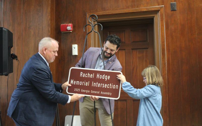 Maeleigh Hodge, right, helps state Rep. Steven Sainz, center, and Camden County Sheriff Kevin Chaney unveil a replica of the sign recognizing Maeleigh’s mother, Rachel Hodge, who died April 18, 2020. Rachel Hodge was a 911 dispatcher for the Camden County Sheriff’s Office.