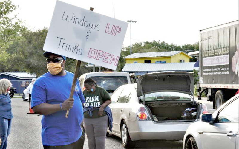 A volunteer holds a sign reminding Farm Share food recipients to keep their windows up and trunks open to help minimize contact and prevent the spread of the coronavirus. ELM STREET SPORTSMAN ASSOCIATION