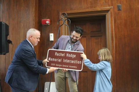 Maeleigh Hodge, right, helps state Rep. Steven Sainz, center, and Camden County Sheriff Kevin Chaney unveil a replica of the sign recognizing Maeleigh’s mother, Rachel Hodge, who died April 18, 2020. Rachel Hodge was a 911 dispatcher for the Camden County Sheriff’s Office.