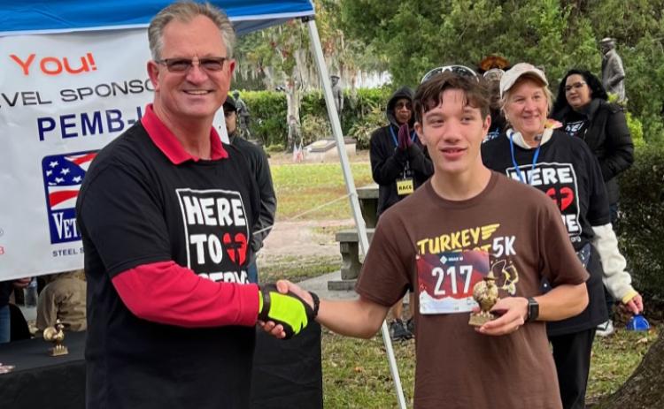 Reiley English, shown with race coordinator Brian Andersen, was the first to cross the finish line with a time of 18:30.