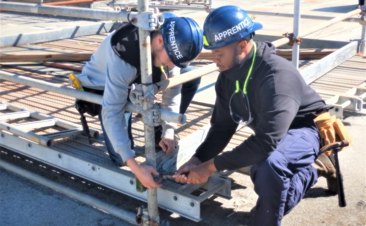 Two Kings Bay Trident Refit Facility apprentices work to set up scaffolding to support repair work on submarines.