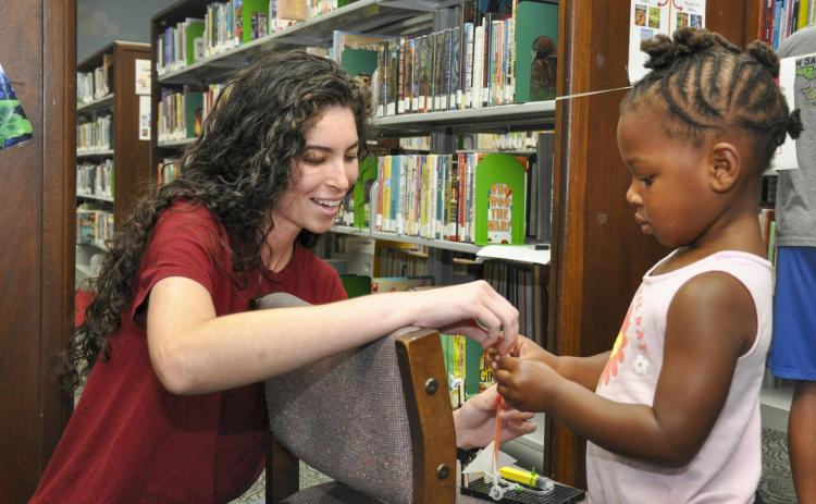 Evelyn Ashe, a Strategic Weapons Facility, Atlantic (SWFLANT) engineering student intern, helps a child prepare her straw missile for launch June 28 at the Camden County Public Library in Kingsland. A team of volunteers from SWFLANT, Lockheed Martin and General Dynamics hosted the event during the Science, Technology, Engineering and Mathematics (STEM) day of the library’s summer learning series.