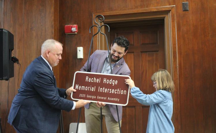 Maeleigh Hodge, right, helps state Rep. Steven Sainz, center, and Camden County Sheriff Kevin Chaney unveil a replica of the sign recognizing Maeleigh’s mother, Rachel Hodge, who died April 18, 2020. Rachel Hodge was a 911 dispatcher for the Camden County Sheriff’s Office.