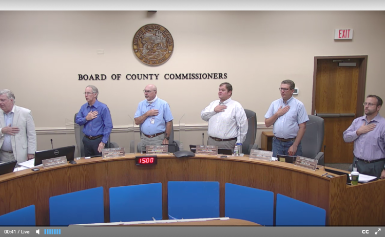 The members of the Nassau County Board of County Commissioners and County Manager and Attorney Mike Mullin stand at attention Wednesday during the Pledge of Allegiance. PEG DAVIS/NEWS-LEADER